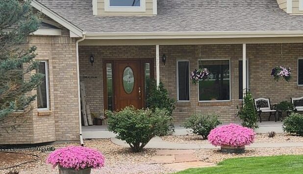 The inviting entrance of Denver Guest Home with a brick facade, flowering plants, and a cozy porch.