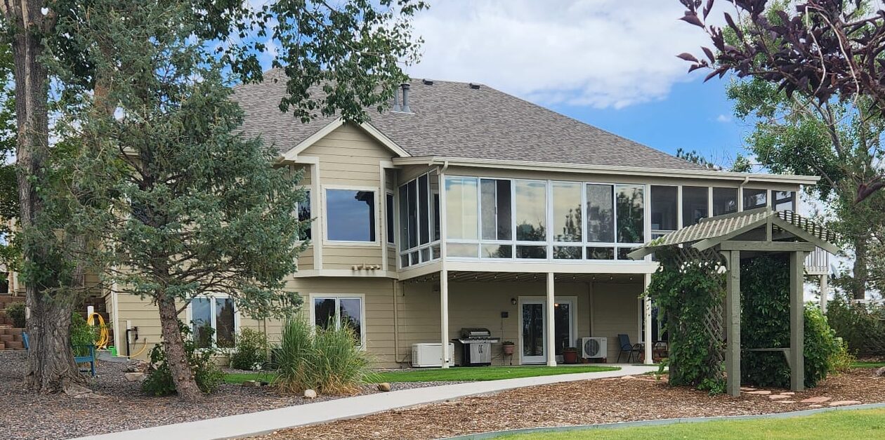 Exterior view of a two-story Denver Guest Home with large glass windows, surrounded by trees and landscaping, featuring a wooden arbor near the entrance.